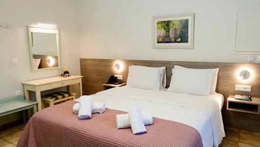 Hotellrum med en dubbelsäng bäddad med vita sängkläder och rosa överkast, handdukar placerade ovanpå sängen, ett skrivbord med spegel och nattlampor vid sidosängarna. (AI-genererad text)