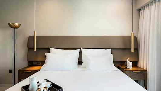 Ett sovrum med en dubbelsäng, ett vitt sänglinne och en bricka med teutrustning på sängen. Lampor och nattduksbord finns på båda sidor. (AI-genererad text)