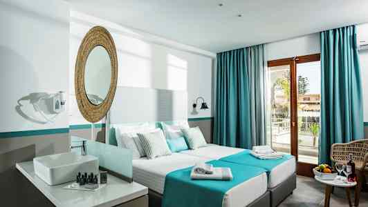 Ett hotellrum med två enkelsängar, en spegel ovanför ett handfat, och en balkongdörr med blå gardiner. (AI-genererad text)