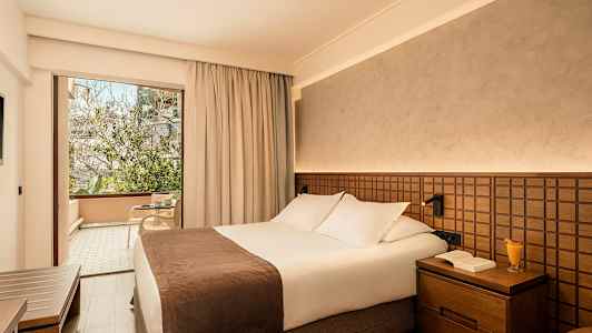 Hotellrum med en dubbelsäng och en glasdörr som leder till en möblerad balkong. (AI-genererad text)