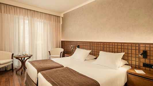 Ett hotellrum med två enkelsängar, brun inredning och en liten sittgrupp. (AI-genererad text)