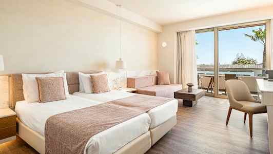 Rum med ljus inredning, två sängar och en sittgrupp vid en terrass. (AI-genererad text)