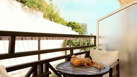 En balkong med ett bord, stolar och en utsikt över grönska. (AI-genererad text)