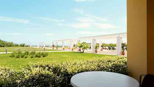 Vy från en terrass med ett runt bord mot en gräsmatta och pergola i bakgrunden. (AI-genererad text)