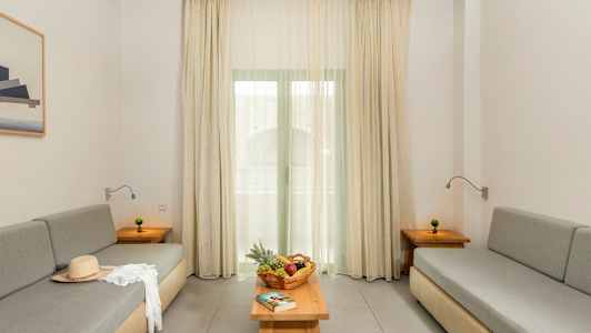 Ett vardagsrum med två grå soffor, ett bord med fruktkorg och en bok, samt gardiner framför fönstret. (AI-genererad text)