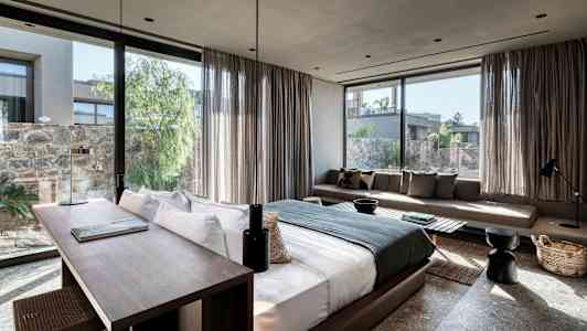 Bild av ett modernt hotellrum med stor säng, skrivbord och soffa, samt fönster med utsikt mot en grönskande innergård. (AI-genererad text)