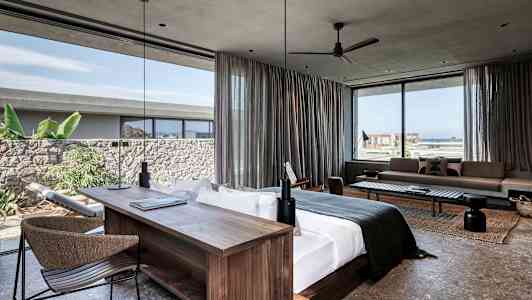 Modern hotellsvit med stor säng, skrivbord och sittutrymme. Fönster med utsikt mot havet och grönska. (AI-genererad text)