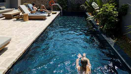 Person simmar i en pool med solstolar vid sidan. (AI-genererad text)