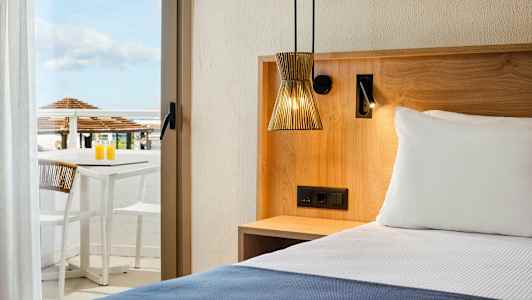 Hotellrum med en säng, träinredning, och en terrass med bord och stolar i bakgrunden. (AI-genererad text)