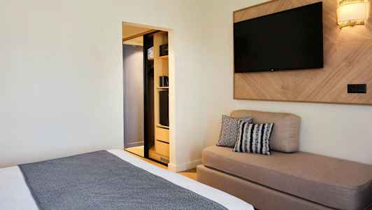 Ett hotellrum med en säng, en soffa, en väggmonterad TV och en öppen garderob. (AI-genererad text)