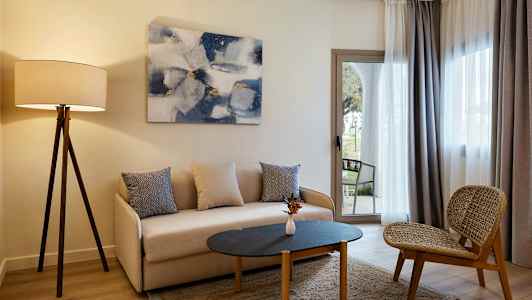 Ett vardagsrum med en soffa, ett bord och en stol, samt en golvlampa och gardiner framför fönstret. (AI-genererad text)