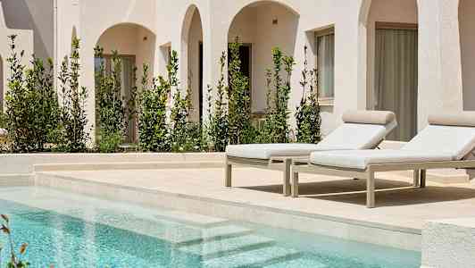 Bild på två solstolar vid en pool, med vita byggnader och gröna växter i bakgrunden. (AI-genererad text)