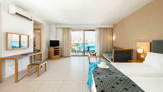 Ett hotellrum med en dubbelsäng, sittmöbler, TV och en balkong med utsikt. (AI-genererad text)