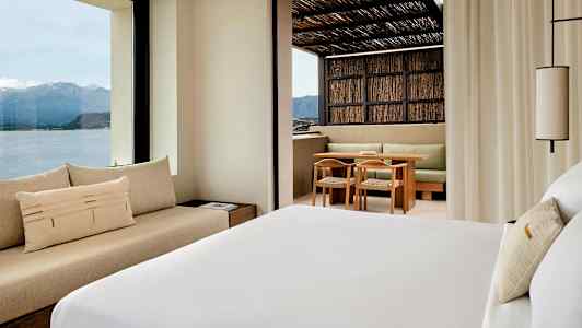 Ett hotellrum med utsikt över berg och hav, samt en terrass med sittgrupp. (AI-genererad text)