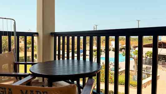 Utsikten från en balkong med bord och stolar med en pool och omgivande byggnader i bakgrunden. (AI-genererad text)