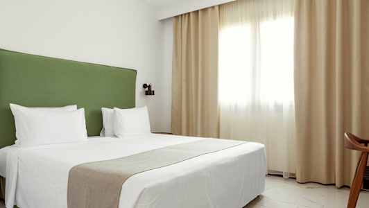 En hotelldubbelrum med en grön sänggavel och vita sängkläder. (AI-genererad text)