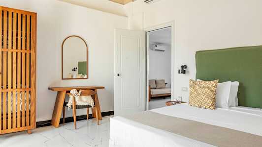 Ett sovrum med en grön sänggavel, en träskrivbord med en spegel ovanför och en trädetaljerad garderob. (AI-genererad text)