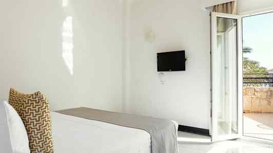 Ett hotellrum med en säng, en väggmonterad TV och en balkongdörr. (AI-genererad text)