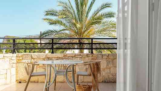 Utsikt över en solig terrass med bord och stolar, mot en palm och blå himmel. (AI-genererad text)