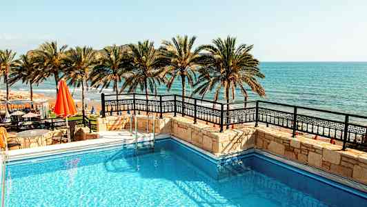 Bild av en pool med havet och palmer i bakgrunden. (AI-genererad text)