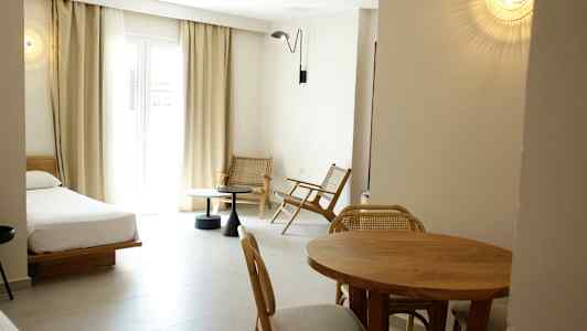 Ett hotellrum med en säng, matbord och stolar, samt en sittgrupp vid ett stort fönster. (AI-genererad text)