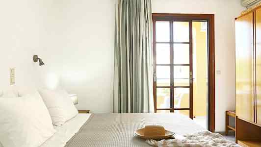 Ett sovrum med en säng, kuddar och en filt. Ett fönster med gardiner och ett nattduksbord syns. (AI-genererad text)