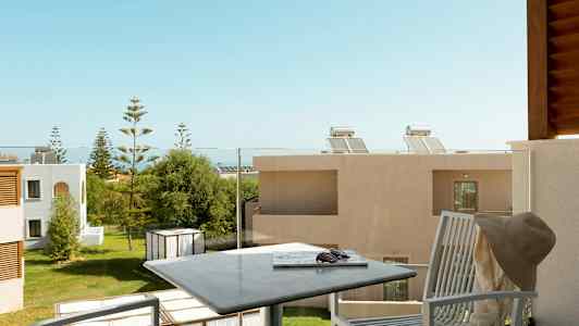 En balkong med sittmöbler och utsikt över en grön trädgård omgiven av byggnader. (AI-genererad text)