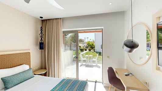 Sovrum med säng, skrivbord och glasdörr till terrass med utemöbler. (AI-genererad text)