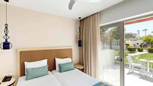 Ett hotellrum med två enkelsängar och fönster som vetter mot en grönskande trädgård. (AI-genererad text)