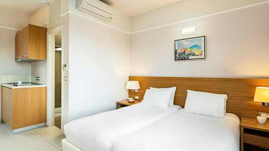 Hotellrum med två sängar, nattduksbord och ett litet pentry. (AI-genererad text)