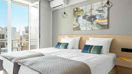 Ett hotellrum med två enkelsängar och en öppen balkongdörr. (AI-genererad text)