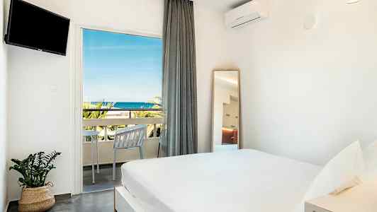 Ett ljust sovrum med en dubbelsäng, en TV på väggen och en balkong med havsutsikt. (AI-genererad text)