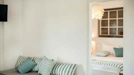 Ett hotellrum med en soffa med kuddar i förgrunden och en bäddad säng i bakgrunden. (AI-genererad text)