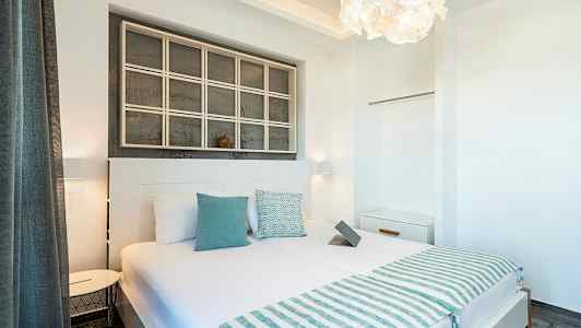 Ett ljust och modernt hotellrum med en dubbelsäng, sänglampor, vita väggar och dekorativa detaljer. (AI-genererad text)