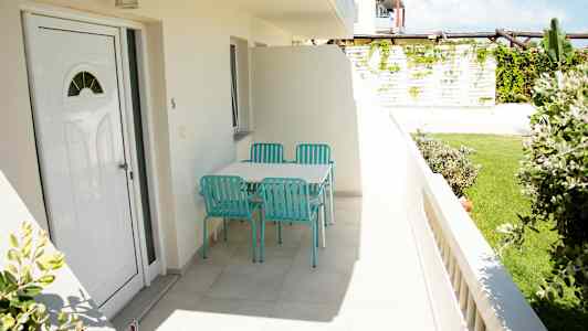 Foto av en terrass med ett bord och fyra turkosa stolar, omgiven av grönska. (AI-genererad text)