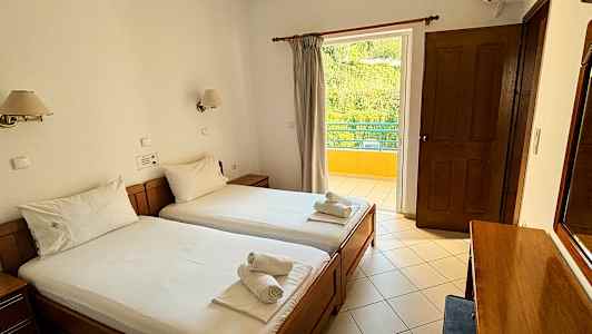 Ett hotellrum med två enkelsängar och handdukar placerade ovanpå. Rummet har en balkong med utsikt över grönska. (AI-genererad text)