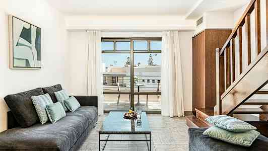 Ett vardagsrum med en soffa, ett bord och en trappa, samt en balkong med utsikt. (AI-genererad text)