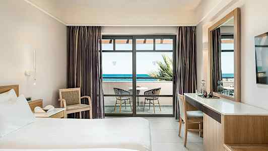 Hotellrum med säng, skrivbord och balkong med havsutsikt. (AI-genererad text)