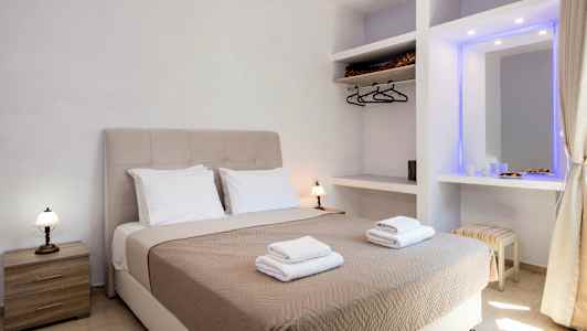 Ett hotellrum med en dubbelsäng utrustad med beige sängöverkast och två uppsättningar handdukar, samt sidobord och garderob. (AI-genererad text)