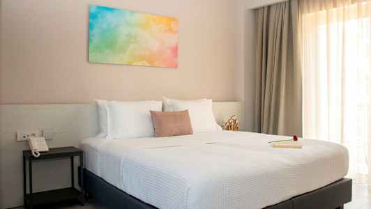 Ett sovrum med en dubbelsäng, vita sängkläder och färgglad tavla på väggen. (AI-genererad text)