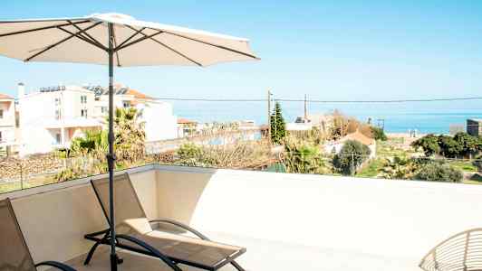 Solstolar och parasoll på en terrass med utsikt över havet och omgivande byggnader. (AI-genererad text)