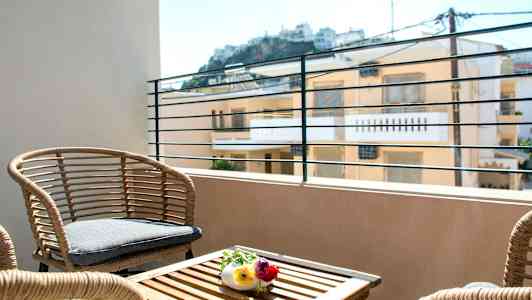 En terrass med rottingmöbler och utsikt mot byggnader i bakgrunden. (AI-genererad text)