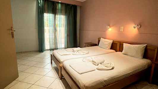 Ett hotellrum med två enkelsängar, bäddade och upplysta av vägglampor, samt ett fönster med gröna gardiner. (AI-genererad text)