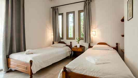 Ett rum med två enkelsängar, en nattduksbord mellan, vita sängkläder och grå gardiner över fönstren. (AI-genererad text)