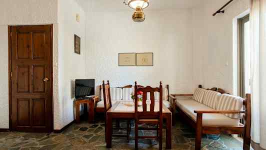 Ett rum med ett träbord och stolar, en soffa samt en dörr och ett tv på ett träbord. (AI-genererad text)