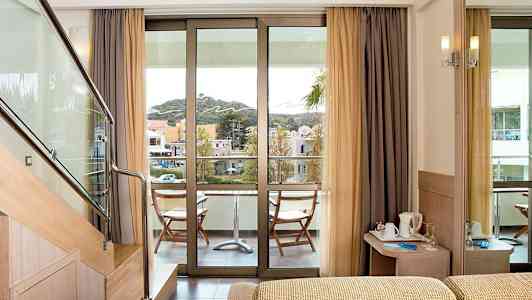 Hotellrum med en balkong med utsikt över omgivningen. Trappor leder till en högre nivå. En liten sittgrupp finns på balkongen. (AI-genererad text)