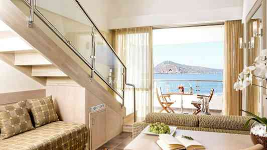 Ett modernt rum med en trätrappa, sittmöbler och en utsikt mot havet från en uteplats. (AI-genererad text)