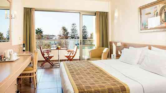 Hotellrum med en dubbelsäng, skrivbord, sittmöbler och en balkong med två stolar och ett bord. (AI-genererad text)