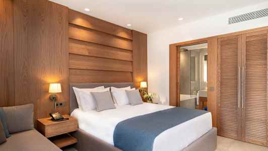 Ett hotellrum med en dubbelsäng, träpaneler på väggen och en glädst dörr som leder till badrummet. (AI-genererad text)