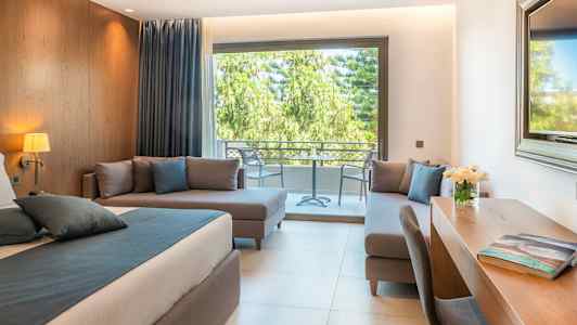 Modernt rum med säng, skrivbord och sittgrupp, utsikt mot uteplats med grönska. (AI-genererad text)